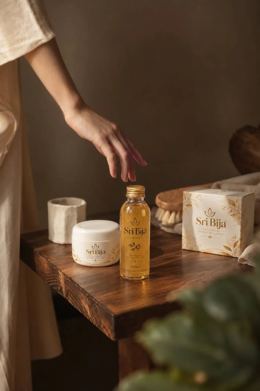 Sri Bija bottle, herbal powder jar and botanical box on a wooden table, with a hand reaching towards the bottle
